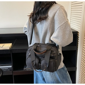 Detail view of a black multi-pocket crossbody bag featuring brown leather trim handles
