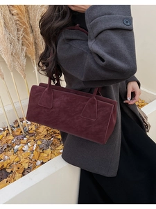 Détail d'un sac bandoulière en daim bordeaux porté avec un manteau en laine en automne