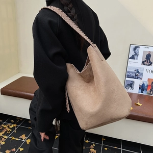 Detail of woven leather strap on a large tan suede hobo bag styled with a black coat