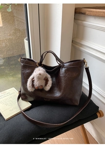 Detail of vintage dark brown tote bag with gold hardware and plush bunny charm on a chair