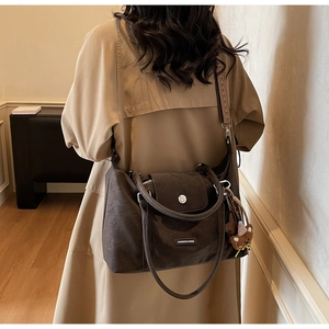 Detail view of large brown vintage tote bag with woven strap and bear charm on khaki coat