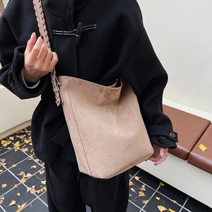Detail of a beige suede tote bag featuring a thick woven shoulder strap and bucket design