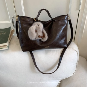 Detail of vintage brown tote bag with plush rabbit charm on a minimalist sofa