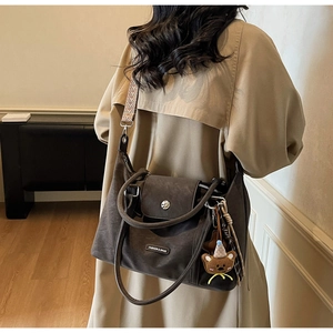 Detail of dark brown matte tote bag featuring ethnic woven strap and cute bear charm