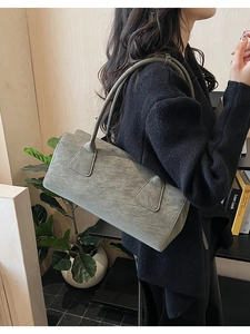 Détail du sac polochon gris en cuir texturé vintage porté à l'épaule dans une pièce