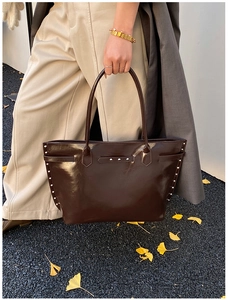 Detail of a large brown glossy leather tote bag with silver rivets held by a model
