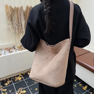 Detail of khaki suede bucket bag with woven strap shown on a black winter coat