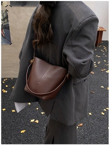 Detail of dark brown pebble leather bucket bag featuring a side metallic buckle and thin strap