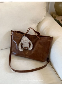 Detail of dark brown vintage oil wax leather tote bag with plush rabbit on creamy sofa