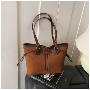 Détail d'un sac cabas en daim marron avec garniture en cuir sur un banc noir minimaliste