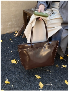 Detailed view of silver rivets on dark brown glossy leather tote bag with long handles