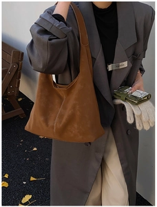 Detail of a brown suede tote bag with white stitching on a background of autumn leaves