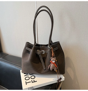 Close-up of brown suede tote bag featuring belt buckle detail and plush bear charm