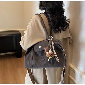 Detail of dark brown matte tote bag featuring cute bear charm and fashion label