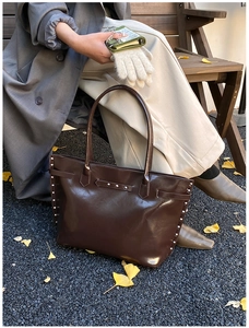 Detail of dark brown leather tote bag with silver metal rivets on outdoor autumn bench