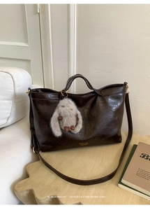 Close-up of dark chocolate leather tote bag with gold brand logo and cute plush bunny charm