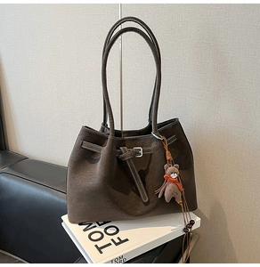 Detail of dark brown suede tote bag with white stitching and bear charm on a book
