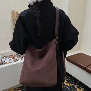 Brown suede tote bag with woven wide strap shown on shoulder in a minimalist setting
