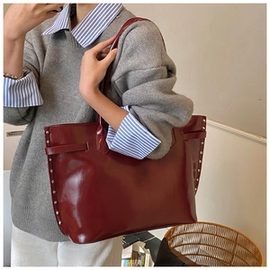 Close-up of wine red patent leather tote bag with silver rivets and buckle detail