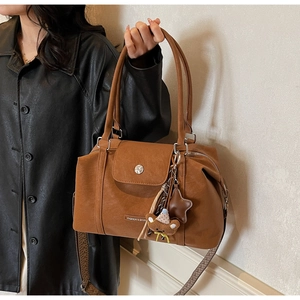Brown retro tote bag with wide geometric strap and plush bear charm on model in black leather jacket