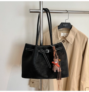 Detail of black tote bag with white stitching and bear charm on a coat hanger