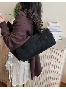 Détail d'un sac à bandoulière minimaliste en daim noir porté par un mannequin en intérieur