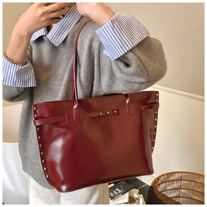 Close-up of wine red tote bag featuring silver rivet studs and polished leather texture