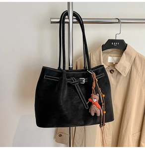 Close-up of black leather tote bag featuring contrast white stitching and cute bear charm