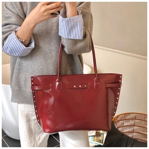 Detail shot of a deep red tote bag featuring metal rivets and glossy leather texture