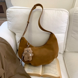 Close-up of brown crescent hobo bag with a cute bear charm on a soft white sofa