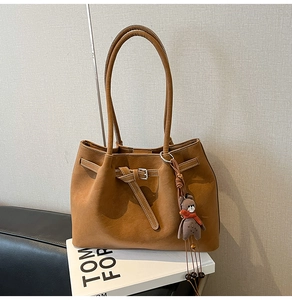 Close-up of caramel brown tote bag featuring matte leather and bear charm on books
