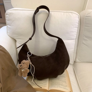 Close-up of dark brown suede crescent bag with adjustable strap and cute bear pendant