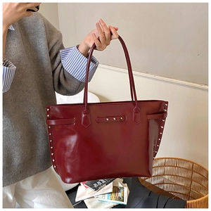Detail of burgundy tote bag showing glossy leather texture and silver rivet studs on the side