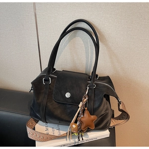 Detail of black leather tote bag with woven shoulder strap and metal buckle