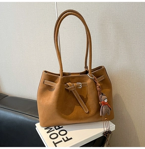 Detail of tan leather tote bag with silver buckle and dark brown bear charm on books