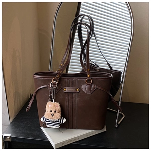 Détails d'un sac cabas en cuir marron foncé avec rayures verticales et charm ours