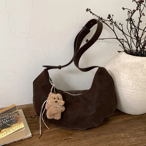 Detail of dark brown suede crescent bag featuring a cute plush bear charm on wooden table