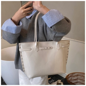 Detailed view of cream leather tote bag with silver rivets and sleek shoulder strap