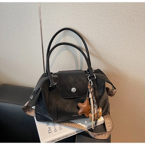 Detail of black leather tote bag with woven shoulder strap and bear charm accessory