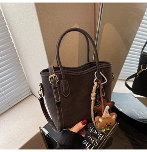 Détail du sac seau mat marron foncé avec surpiqûres contrastées et breloque ours en peluche