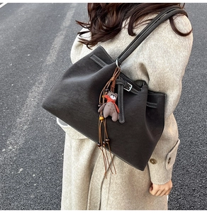 Detail of grey tote bag with bear charm and tassel on a model in beige coat