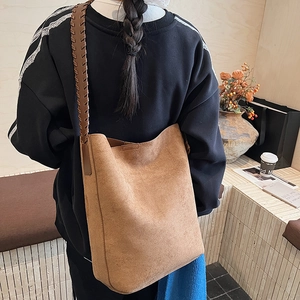 Detail of a brown suede tote bag featuring a decorative wide hand-woven shoulder strap
