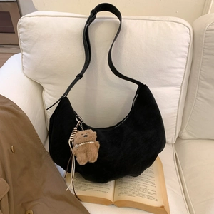 Detail of black suede crescent bag with cute bear charm on a cozy white fabric sofa