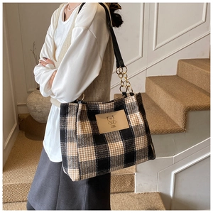 Detail of checkered tote bag featuring a leather bear patch and gold chain strap