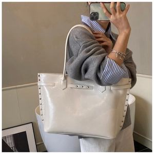 Close-up of white patent leather tote bag featuring silver studs and buckle details