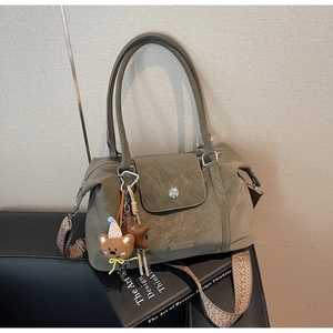 Detail of olive green Boston bag featuring woven strap, matte texture and bear charm