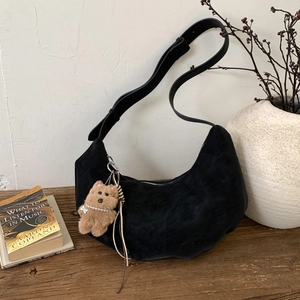 Detail of black suede crescent bag with plush bear charm and long tassel on wooden bench