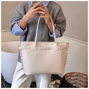Detail view of large white tote bag with metal rivets and smooth synthetic leather texture