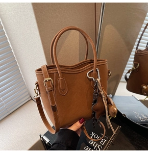 Détail d'un sac seau marron givré avec coutures blanches et charm à pompon élégant