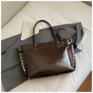 Detail of dark coffee oily leather tote bag with silver stud accents on white fabric
